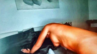 Performer in lingerie sitting on a bed, facing the camera
